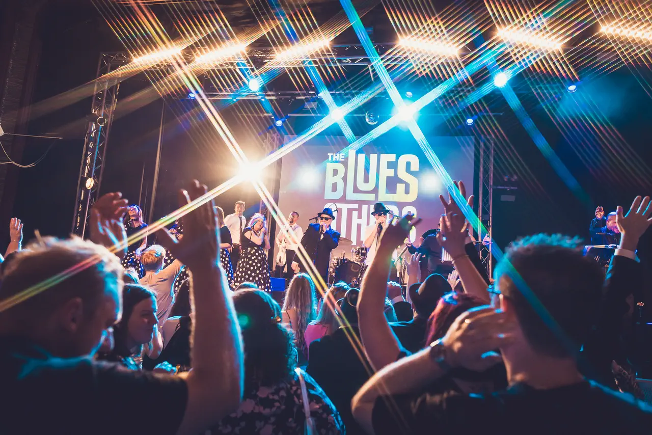Crowd dancing with hands raised in front of The Blues Others on stage